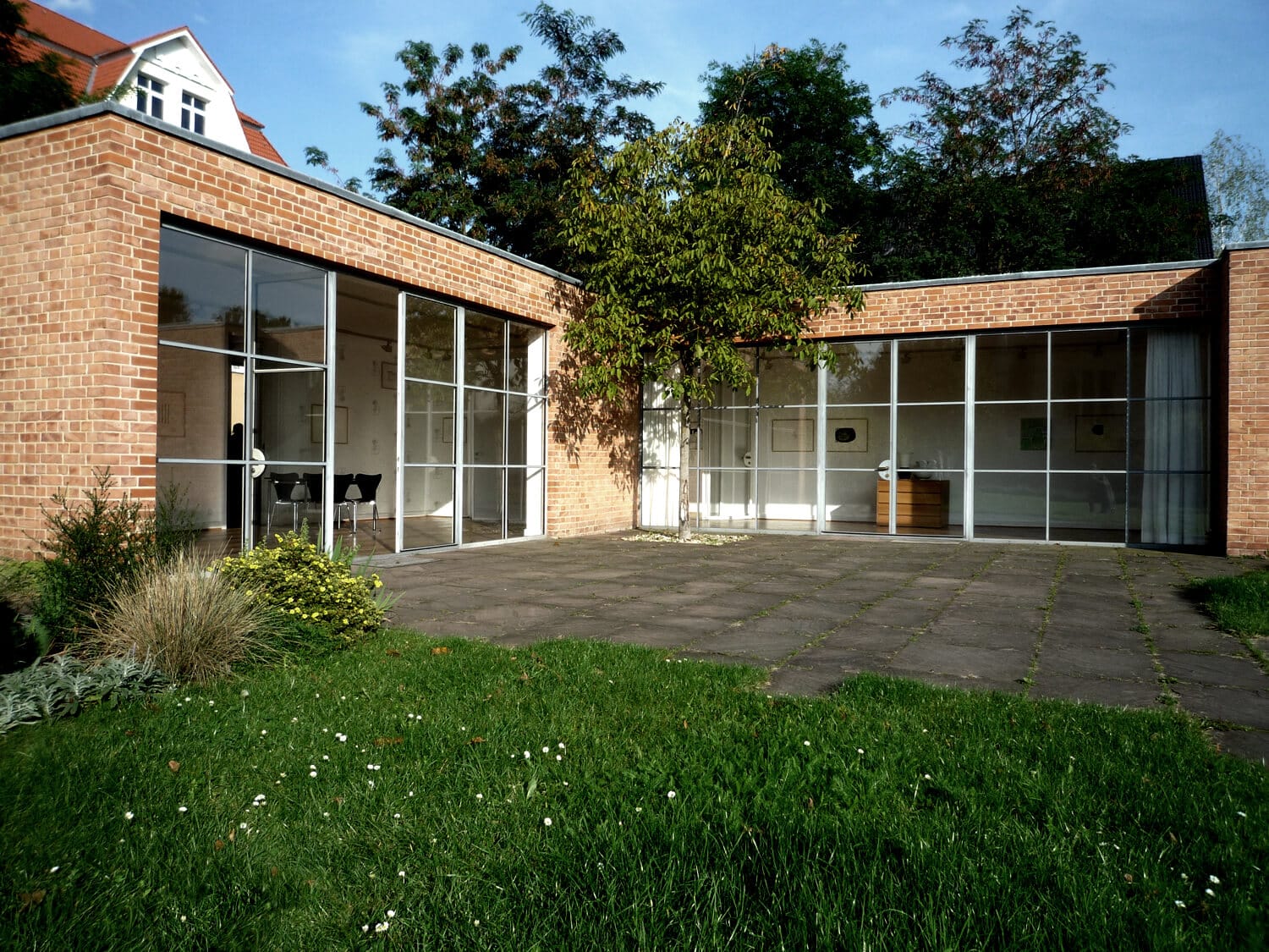 Moderner Bungalow frontal mit Klinkerfassade bodentiefen Fenstern Terrasse und Garten mit Baumpflanzung