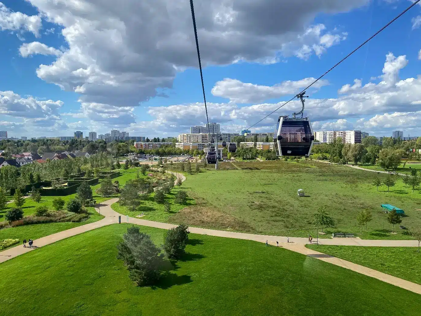 Téléphérique au-dessus d'un parc verdoyant sous un ciel bleu, vue de la ville en arrière-plan, journée ensoleillée.