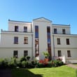Edifício de apartamentos independente, vista frontal, fachada branca, caixilharia de janelas castanha, pequeno jardim com plantas em vasos
