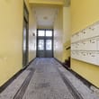 Innenansicht Mehrfamilienhausflur mit gelben Wänden, Pflasterboden, Haustür und Wandbriefkästen rechts