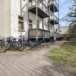 Mehrfamilienhaus Rückseite mit drei Balkonen über Fahrradständern im Innenhof und gepflastertem Weg neben Rasenfläche
