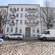 Frontansicht eines viergeschossigen Mehrfamilienhauses mit Balkonen auf Kopfsteinpflaster