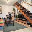 Wohnzimmer mit offener Holztreppe zum Obergeschoss, Sofa, Couchtisch, TV-Möbel und Regalen