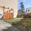 Sonniger Hinterhof mit Rasenfläche und Holzeinhausung für Mülltonnen neben Hauswand und Maschendrahtzaun