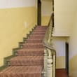 Innenansicht eines Treppenhauses mit gemusterter Teppichstufe und abgenutztem grünen Holzgeländer