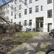 Hinterhofperspektive auf mehrgeschossiges Wohngebäude mit weißer Putzfassade, Vorgarten, Fahrradstellplätzen und Sitzstühlen