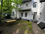 Hinterhofansicht eines Mehrfamilienhauses mit Balkon und bewachsenem Garten