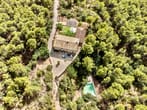Drohnenaufnahme eines Landhauses inmitten dichtem Nadelwald mit gepflastertem Hof und Swimmingpool
