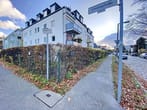 Canto da rua com edifício residencial de vários andares com fachada rebocada, varandas e sebe de contenção a partir de uma perspetiva ao nível do solo