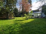Vista de casa unifamiliar com jardim de inverno e zona de terraço, em frente a um extenso relvado e árvores circundantes
