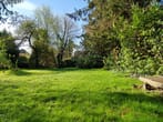 Vista de área relvada num jardim privado rodeado por árvores e arbustos sob o sol