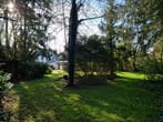 Vista do jardim com relva e árvores para uma casa unifamiliar parcialmente branca à luz do sol