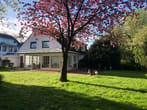 Vista traseira branca de uma casa unifamiliar com jardim de inverno envidraçado no jardim sob uma cerejeira em flor