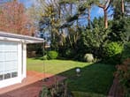 Vista de terraço de tijolo vermelho para estufa branca e jardim verde com relva e árvores