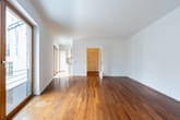 Blick ins helle Wohnzimmer einer Neubauwohnung mit Parkettboden bodentiefen Fenstern Balkon und offener Einbauküche