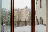 Blick durch geöffnete Terrassentür auf schneebedeckten Balkon mit Metallgeländer und Nachbargebäude