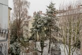Verschneiter Innenhof mit Laub- und Nadelbäumen umgeben von mehrgeschossigen Altbauwohnungen mit kleinen Balkonen