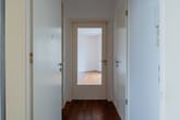 Innenansicht eines Wohnungsflurs mit weißer Haustür links, Glastür geradeaus und dunklem Parkettboden
