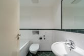 Innenaufnahme Badezimmer mit wandhängendem WC Eckbadewanne Waschbecken Spiegel und grünen Bordüren- und Bodenfliesen