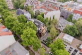 Draufsicht auf modernes Mehrfamilienhaus mit Penthouse-Terrasse, begrüntem Innenhof und umliegendem Baumbestand