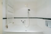 Innenansicht Badezimmer mit weißer Badewanne, verstellbarer Handbrause, grünem Fliesenspiegel und senkrechtem Heizkörper