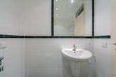 Innenperspektive Badezimmer mit weißem Wandwaschbecken unter großem Spiegel und dunkelgrüner Fliesenbordüre