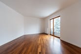 Innenansicht eines leerstehenden Wohnzimmers mit Parkettboden und bodentiefer Fensterfront zum Balkon