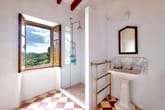 Helles Landhausbadezimmer mit Glasdusche, freistehendem Waschbecken, goldfarbenem Handtuchwärmer und offenem Fenster mit Landschaftsblick