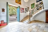 Blick in Eingang eines Einfamilienhauses mit Steinboden geschwungener Treppe und geöffneter Rundbogentür zum Garten