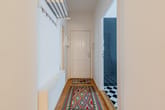 Apartmentflur mit Blick zur weißen Eingangstür Dielenboden bunter Läufer Wandgarderobe und Spiegel