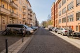Straßenperspektive mit mehrgeschossigen Wohnhäusern mit Balkonen und Klinkerfassade neben geparkten Autos und Fahrrädern