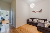 Wohnzimmer aus Eckperspektive mit Holzdielenboden und grauem Ecksofa sowie dreiteiligem Wandbild