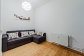 Blick ins Wohnzimmer mit L-Sofa, Holzdielen, Wandheizung, Pendelleuchte und abstraktem Wandbild