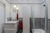 Innenansicht Badezimmer mit Glas-Duschkabine weißem Waschbeckenunterschrank grauen Wandfliesen und Handtuchhaken