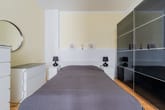 Schlafzimmer frontal mit grauem Einzelbett, rundem Spiegel, weißem Nachttisch und schwarzem Schiebetürenschrank