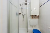 Innenansicht eines Badezimmers mit Glastürdusche wandhängendem Boiler und WC mit blauem Sitz