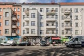 Frontalansicht mehrgeschossiges Wohnhaus mit Balkonen und bunten Graffiti-Läden im Erdgeschoss