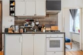 Kompakte Einbauküche in Altbauwohnung von vorne mit Holzfliesenrückwand, weißen Paneelschränken, Gasherd und Kühlschrank