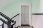 Blick auf historische Paneeltür im Altbauflur mit pastellgrüner Wand und schwarzem Holzgeländer
