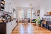Offener Wohn-Küchenbereich in Altbauwohnung mit Dielenboden, zwei Bogenfenstern und Einbauküche