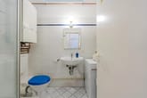 Kompaktes Badezimmer mit weißen Fliesen, blauem Toilettensitz, Waschbecken, Spiegel und Waschmaschine in Frontansicht