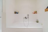 Badezimmer mit eingelassener Badewanne, verchromter Handbrause und seitlichen Nischen mit Pflegeprodukten