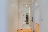 Innenansicht einer Wohnung mit Blick vom Flur in ein Bad weiße Einbauschränke Holzboden und offenes Regal