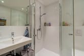 Innenansicht Badezimmer mit ebenerdiger Dusche mit Glasabtrennung Handtuchregal und wandhängendem Waschbecken