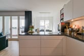 moderne offene Wohnküche mit schwarzer Arbeitsinsel raumhohe Fenster zum Balkon und Esstisch