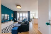 Offener Wohnbereich in moderner Wohnung mit Couch, TV-Wand, Kücheninsel und Balkon mit bodentiefen Fenstern