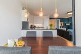 Einblick in offene Wohnküche eines modernen Apartments mit Esstisch, goldenen Pendelleuchten und dunkelgrüner Akzentwand