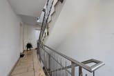 Bina içi apartman merdiven holü, paslanmaz çelik korkuluk, fayans zemin, beyaz duvarlar ve bitki