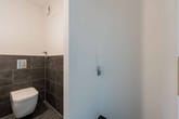 Interior de casa de banho de visitas com sanita suspensa, azulejos cinzento-antracite a meia altura e ligação de água lateral