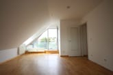 Vista interior de um apartamento no sótão com piso em parquet, teto inclinado e janela de porta aberta para a varanda